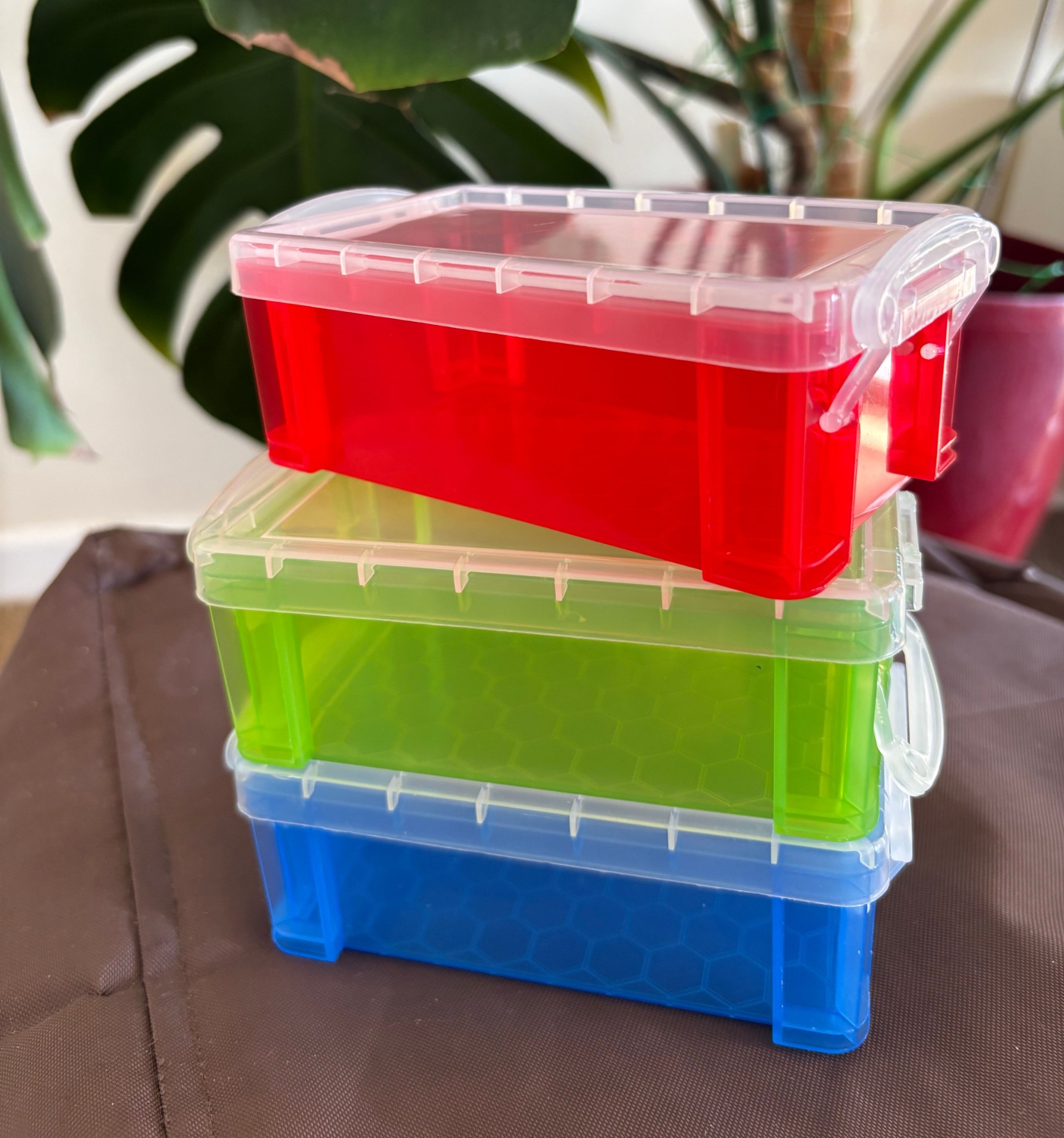 Stacked translucent plastic storage containers in blue, green and red, each with a hinged lid and latch clips.
